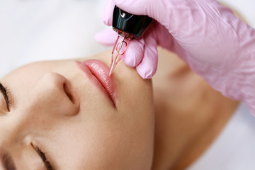 Beautiful young girl in beauty salon. Woman having permanent tattoo makeup on her lips.