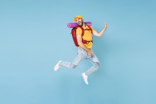 Full Length Portrait Funny Young Traveler Man In Cap With Backpack Isolated On Blue Background. Tourist Traveling On Weekend Getaway. Tourism Discovering Hiking Concept. Jumping Like Playing Guitar.