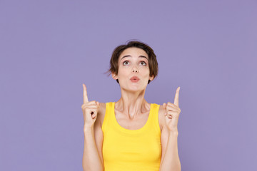 Shocked young brunette woman girl in yellow casual tank top posing isolated on pastel violet wall...