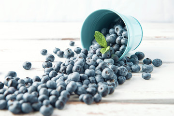 Bucket with scattered blueberry and mint leaves on white Provence style wooden table.