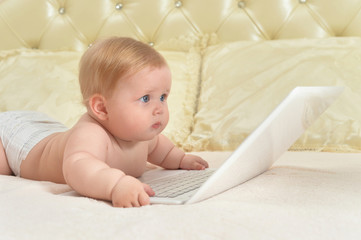 Cute little baby girl on bed with laptop