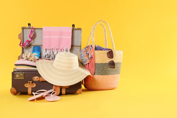 Bag and open vintage suitcase with different beach objects packed for summer vacation on orange...