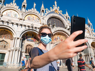 A tourist during the coronavirus pandemic, covid-19. A young woman wears a surgical mask in Piazza San Marco, in the background Cathedral Basilica of Saint Mark. A famous destination in Italy.