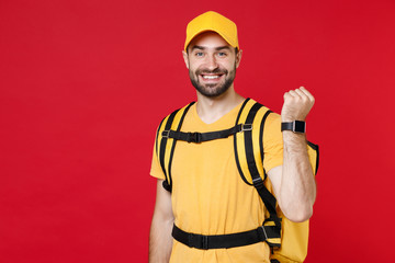 Delivery man in yellow cap t-shirt uniform thermal bag backpack with food hand smartwatch isolated on red background studio Guy male employee work as courier Service coronavirus covid-19 virus concept