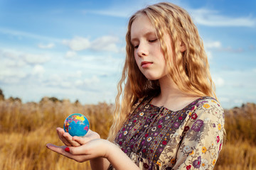 A  girl with curly wheat hairs  holds  toy of the globe , face close-up, on yellow field and blue sky. Travel concept. 