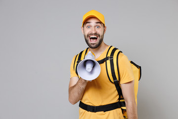 Delivery employee man guy male in yellow cap tshirt uniform thermal food bag backpack work courier service during quarantine coronavirus covid-19 scream in megaphone isolated on gray background studio