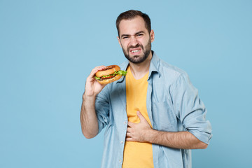 Displeased sick young bearded man guy 20s in casual clothes posing hold american classic fast food...