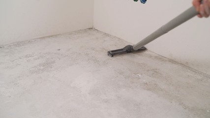Cleaning cement floor with vacuum cleaner. A worker removes dust with a vacuum cleaner. A worker with an industrial vacuum cleaner removes dust from repairs. Floor preparation for renovation.