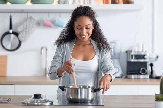 Happy young african american woman cooking healthy food in casserole in the kitchen at home.