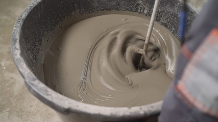 A worker mixes the solution in a bucket. The mortar is mixed with a construction mixer. Floor...
