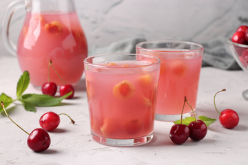 Kissel with sweet cherries in two glasses and jug on gray background, Horizontal format