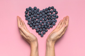 Female hands hold fresh blueberries in the shape of heart on pink background. Blueberries...