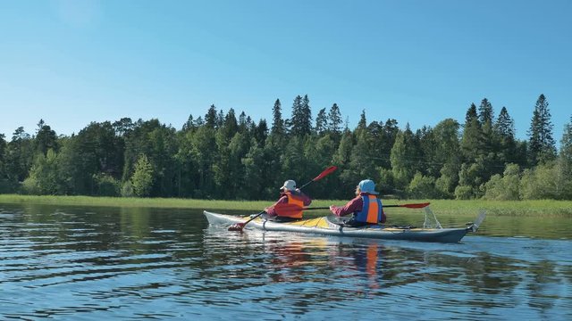 active young man and woman in orange vests sail small plastic kayak along tranquil river on sunny summer day backside view