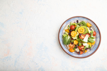 Vegetarian salad of pac choi cabbage, kiwi, tomatoes, kumquat, microgreen sprouts on a white concrete background. Top view, copy space.