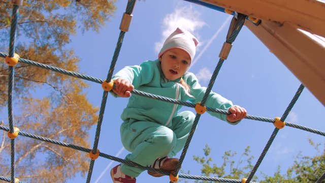 Cute active child climbs and crawls on horizontal rope wall on playground