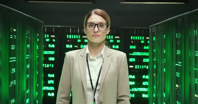 Portrait of young happy Caucasian beautiful woman, worker of database storage smiling while standing with crossed hands. Female good-looking smiled engineer or analytic coming to camera in datacenter.