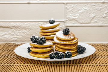 Dessert and breakfast concept. Sugar powder being poured over pancakes.Tasty breakfast food. Stack of american pancakes served with black currant and blackberry