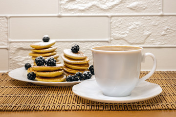 Pancakes with honey, berry fruit and sugar powder and white cup with coffee. Sweet food. Dessert and breakfast concept