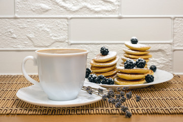 Pancakes with honey, berry fruit and sugar powder and white cup with coffee. Sweet food. Dessert and breakfast concept