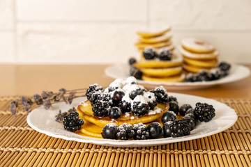 Dessert and breakfast concept. Sugar powder being poured over pancakes.Tasty breakfast food. Stack of american pancakes served with black currant and blackberry