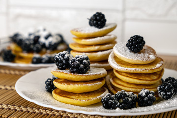 Dessert and breakfast concept. Sugar powder being poured over pancakes.Tasty breakfast food. Stack of american pancakes served with black currant and blackberry