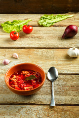 A plate of clay borscht with chicken with a spoon on a wooden table near vegetables.