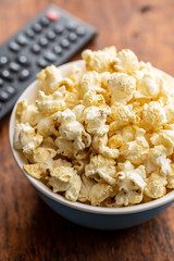 Sweet tasty popcorn in bowl and TV remote control.