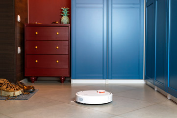 Home Cleaning Concept. Modern robotic vacuum cleaner cleans the porcelain stoneware floor in the hallway. New technologies, quick house cleaning automatic robot assistant. Smart appliance for cleaning