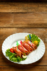 Ham rolls on a plate with green salad on a wooden table. save a place.