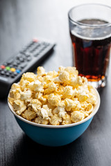 Sweet tasty popcorn in bowl and TV remote control.