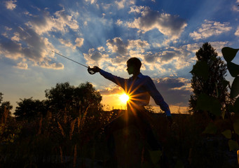Silhouette of a man with a saber against the background of sunrise or sunset. Freedom fight concept. Outdoor fencing training.