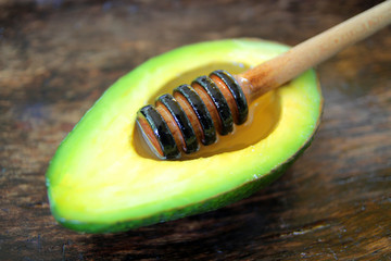 
honey dipper with natural honey lies on a slice of avocado in a wooden plate.
