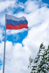 Russian tricolor flag waving in the wind against a cloudy sky.