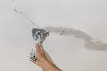 Worker fixing cracks on ceiling, spreading plaster with trowel, selective focus
