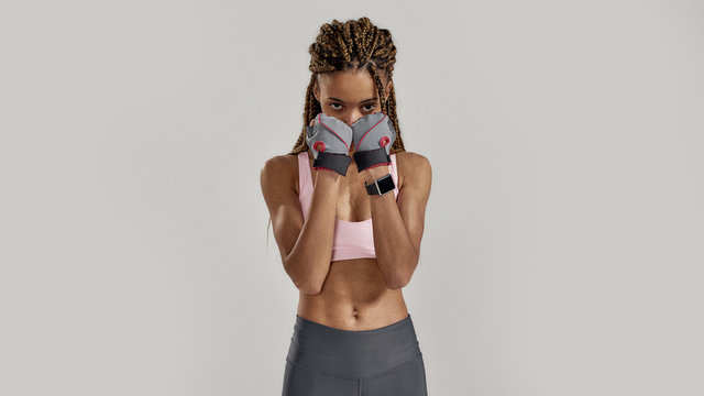 Portrait of young sportive mixed race woman in sportswear looking at camera, wearing fitness gloves while posing isolated over grey background. Healthy lifestyle and sports concept