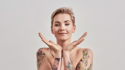 Portrait of half naked tattooed woman with short hair looking at camera, holding open palms under...