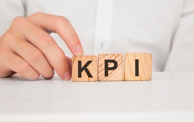 Naklejka premium Close up young man's hand in white shirt wooden block cube for Kpi wording on white marble table floor