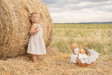 toddler blond girl in linen dress in field of hay with basket of bread and milk.