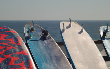 Pranchas de surf encostadas numa vedação de uma praia com o mar e linha de horizonte de fundo