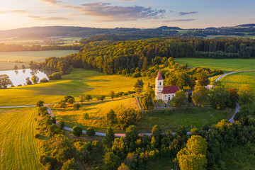 Naklejka premium Church on the hill with sunlit summer landscape from above. Bysicky church near SPA town Lazne Belohrad, Czech Republic. Sunset gold light.