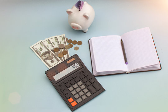 On a blue background, there is a notebook, a calculator, bills, coins and a piggy bank. Horizontal photo artistically processed Idea for planning your monthly expenses Business concept