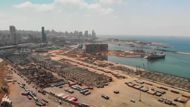 Aftermath of the Beirut port explosion, featuring a damaged grain silo, twisted metal structures, and scattered debris amid ongoing reconstruction efforts.