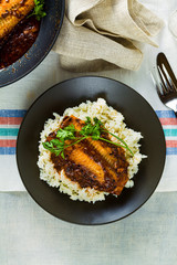 fillet of pink salmon in tomato-coconut sauce in a non-stick frying pan with parsley on a table with a linen tablecloth. healthy family food with basmati rice