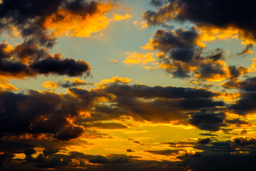 A very dramatic sky full of yellows, blues and oranges. Contrasting clouds during sunset illuminated by the setting sun. Bright saturated natural background. High quality photo