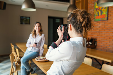 Female professional photographer taking picture of young woman in room