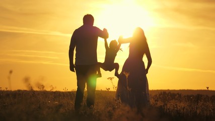 mom, dad and baby play outdoors. healthy little daughter jumps and flies in arms of mother and father in field at sunset. Happy family walks in field in sun. concept of happy family of children.