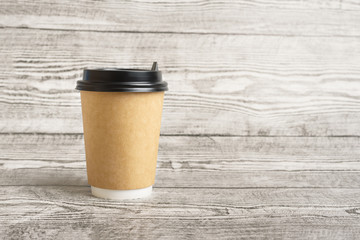 One eco friendly paper craft cup for coffee or tea with black lids on the wooden background. Zero waste, plastic free concept. Sustainable lifestyle. Front view.