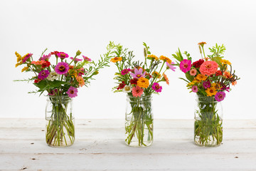 Colorful summer wildflowers in a clear jar on an old wooden table isolated on white with a shallow depth of field