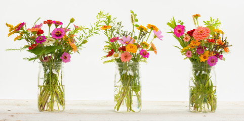 Colorful summer wildflowers in a clear jar on an old wooden table isolated on white with a shallow depth of field