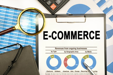 The businessman has on his desk graphs with reports, a notebook, a magnifying glass and a document with the inscription - E-COMMERCE